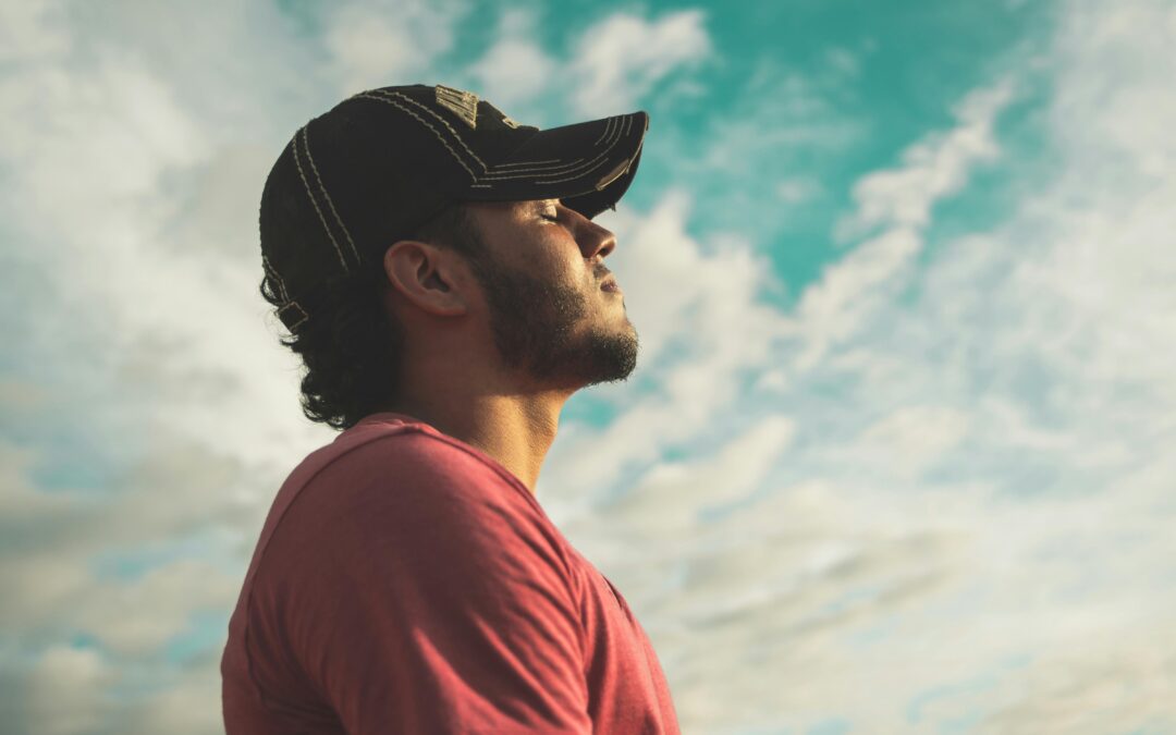 photo of a man wearing a black cap with eyes closed under cloudy a sky