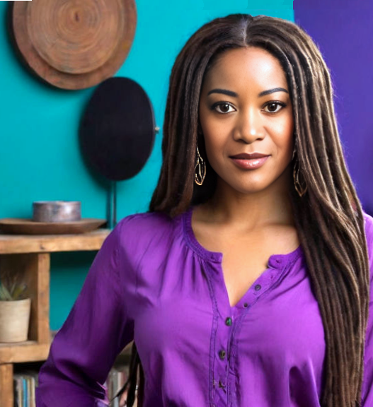 A woman with long brown locs is wearing a purple blouse. There is a teal colored wall with a shelf in the background.